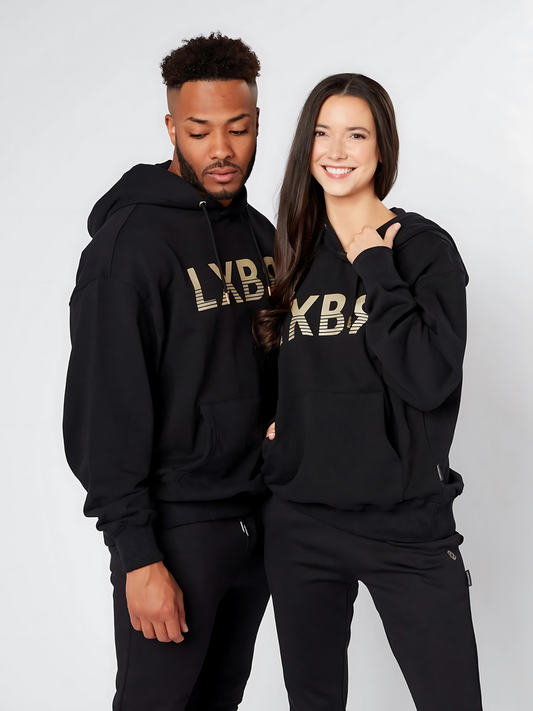 A man and a woman standing side by side, both wearing black unisex oversized hoodies with the text 'LXBR' on the front - Lexanber UK